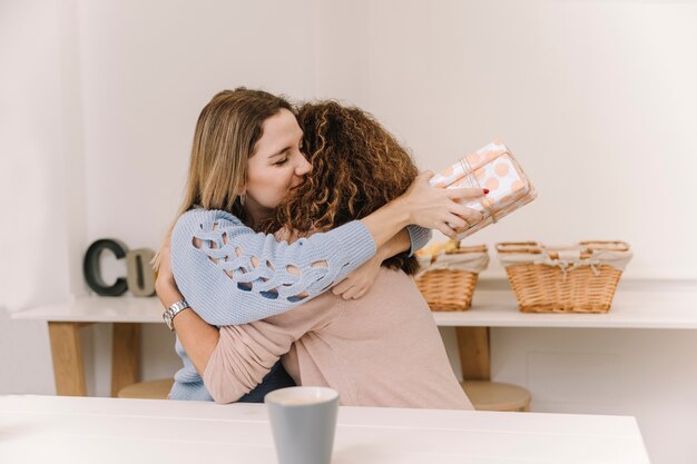 Woman with gift hugging mother during breakfast