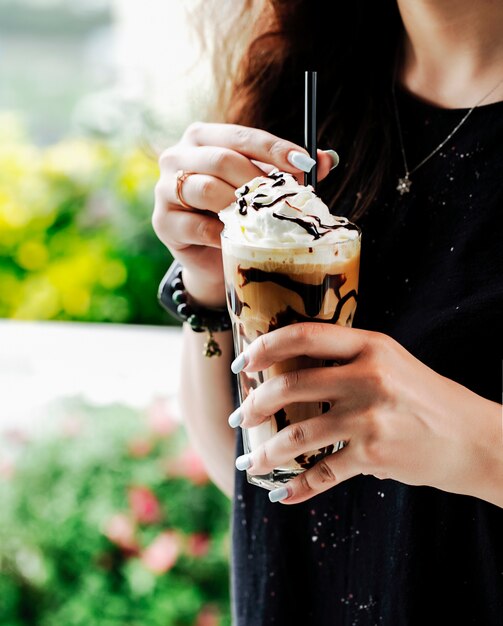 Woman with a glass of coffee smoothie with chocolate syrup and ice cream ball.