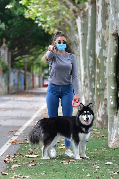 Woman with glasses and surgical mask holding a dog on a leash pointing towards the camera