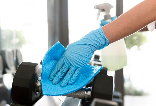 Woman with gloves disinfecting weights at the gym