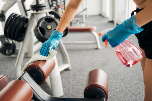 Foto gratuita donna con guanti in palestra disinfettando attrezzature