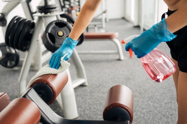 Woman with gloves at the gym disinfecting equipment