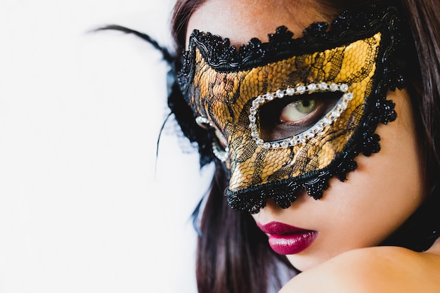 Woman with a golden venetian mask and a black hat on a white background