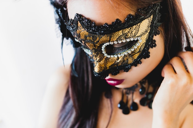 Woman with a golden venetian mask and a black hat on a white background