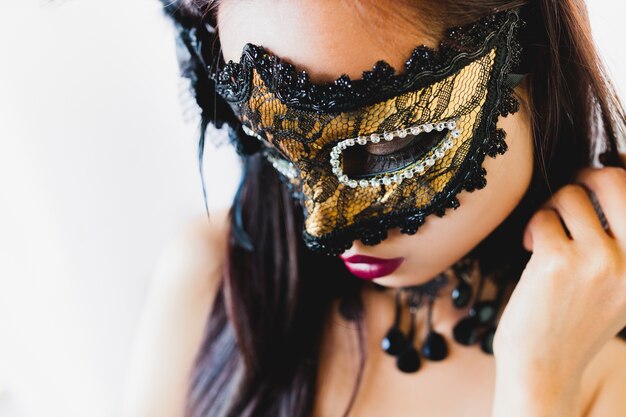 Woman with a golden venetian mask and a black hat on a white background