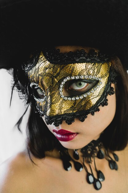 Woman with a golden venetian mask and a black hat on a white background