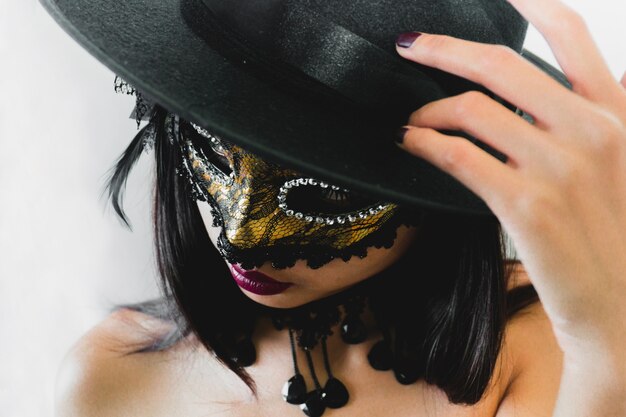 Woman with a golden venetian mask and a black hat on a white background