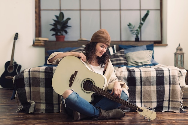 Free photo woman with guitar in front of bed