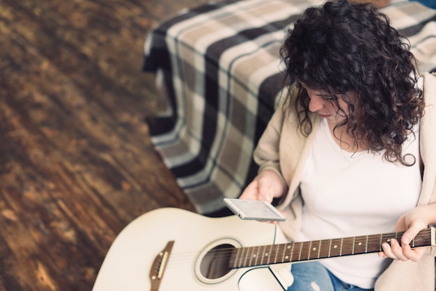 Foto gratuita donna con chitarra guardando smartphone