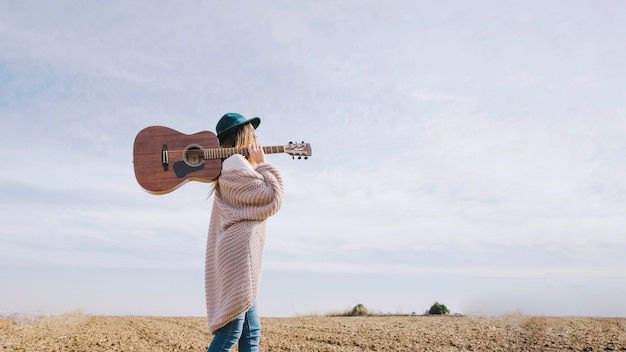 Foto gratuita donna con la chitarra che cammina in campagna