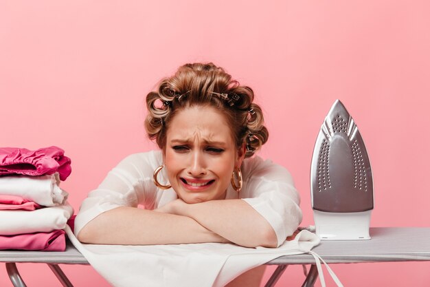 woman with hair curlers leans on ironing board and cries