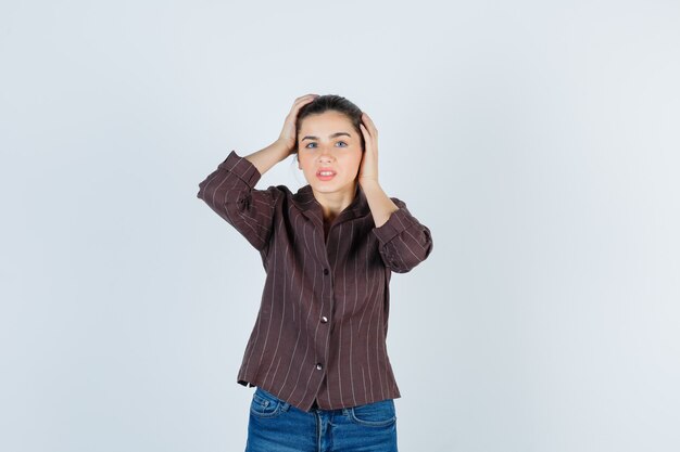 woman with hands on head in brown striped shirt and looking troubled , front view.