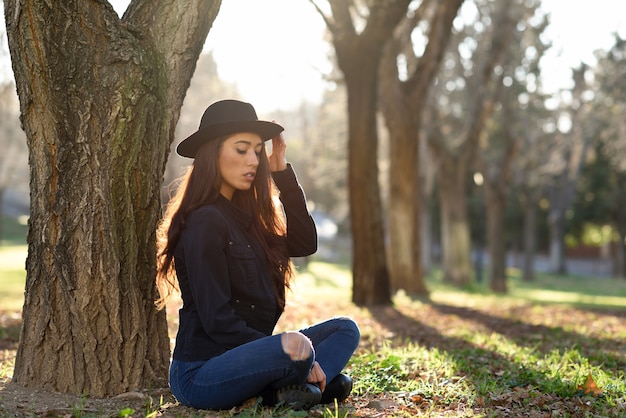 Woman with a hat sitting and leaning on a tree