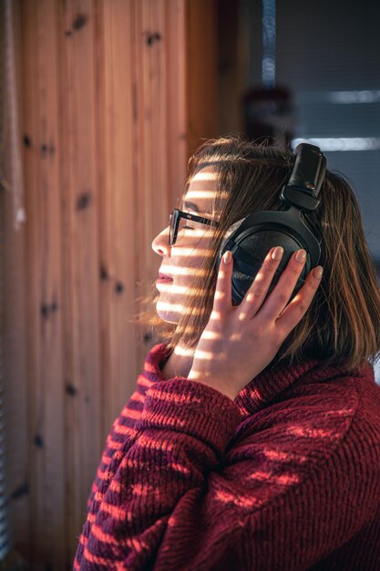 A woman with headphones looks through the blinds at the early morning sunlight