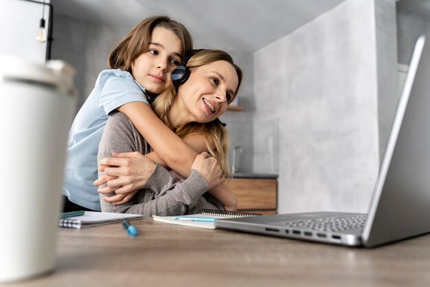 Woman with headset working on laptop hugged by girl