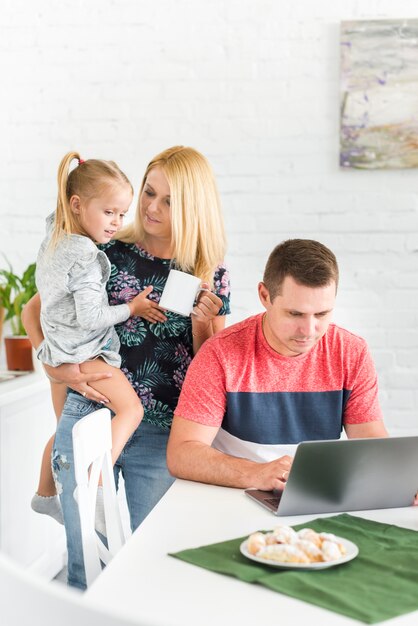 Woman with her daughter standing behind her husband using laptop
