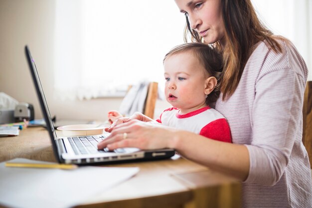 Woman with her kid working on laptop over wooden desk