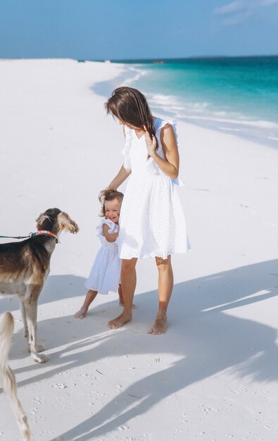 Woman with her little daughter playing with dogs at the beach by the ocean