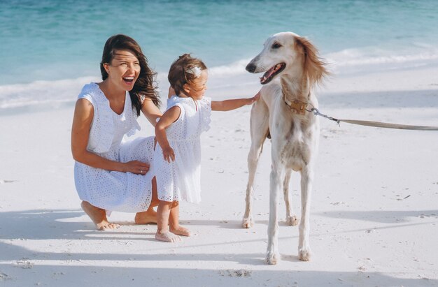 Woman with her little daughter playing with dogs at the beach by the ocean