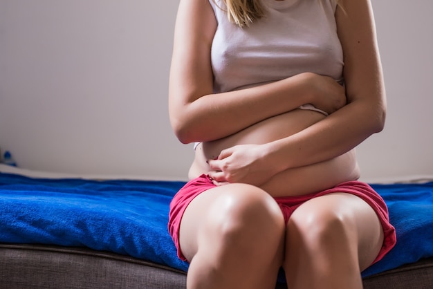 Woman with her monthly menstrual pains clutching her stomach with her hands as she becomes stressed by the ongoing cramps, torso view of her hands and tummy