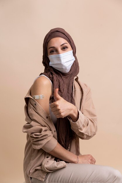 Woman with hijab showing sticker on arm after getting a vaccine