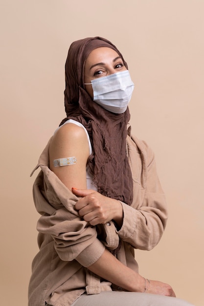 Woman with hijab showing sticker on arm after getting a vaccine