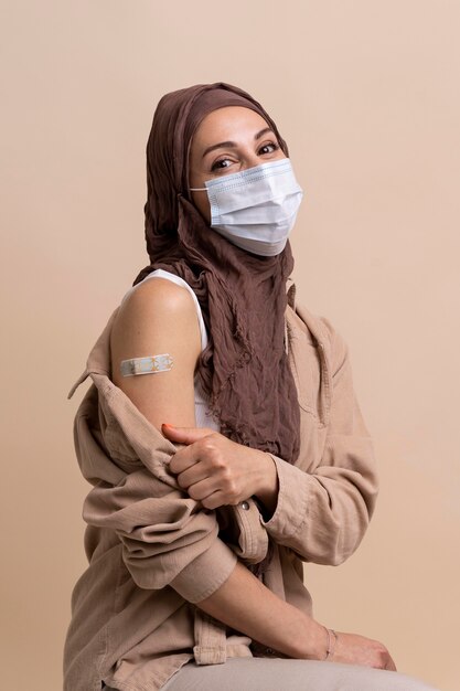 백신 접종 후 팔에 스티커를 보여주는 히잡을 가진 여자