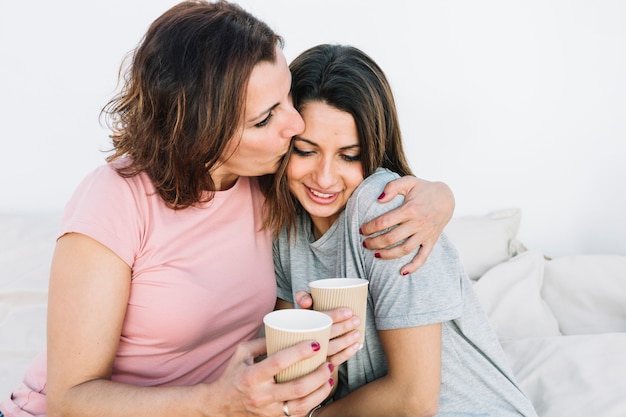 Woman with hot drink kissing woman