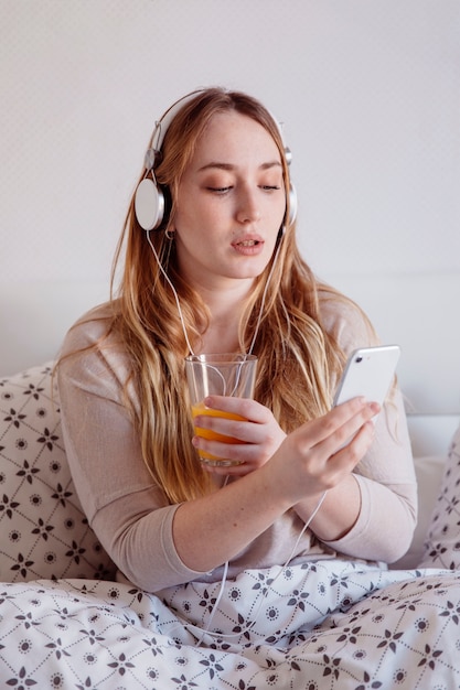 Free photo woman with juice browsing smartphone in bed