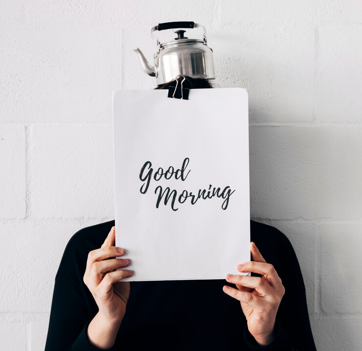Free Photo woman with kettle over head and good morning message on paper holding in front of face against white wall