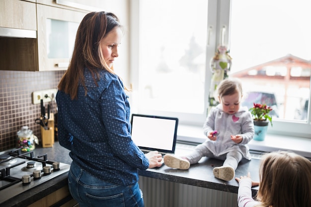 Donna con il portatile guardando i suoi figli in cucina