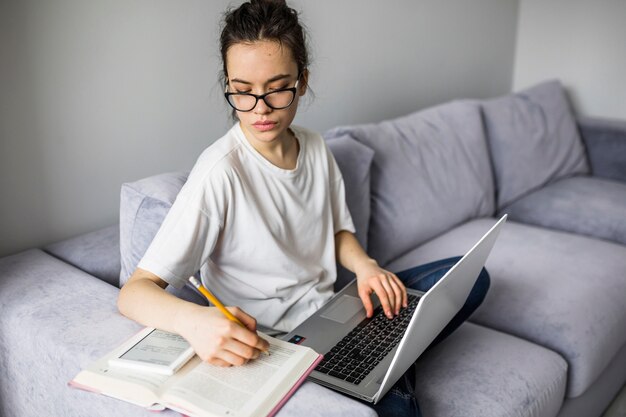 Woman with laptop making notes in book