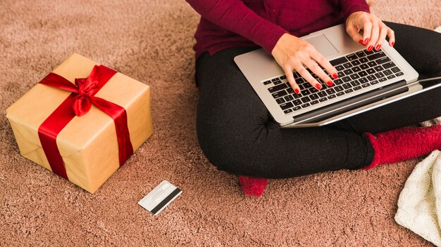 Woman with laptop near plastic card and gift box