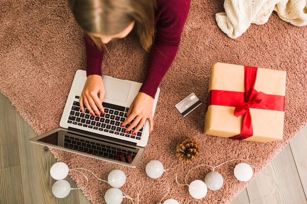Woman with laptop near plastic card, present box, snag and fairy lights 