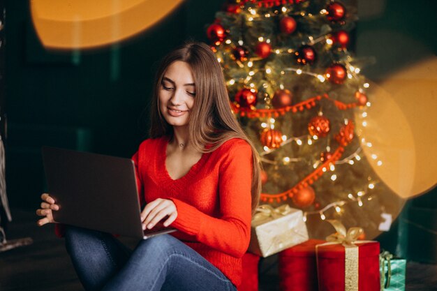 woman with laptop sitting next to christmas tree