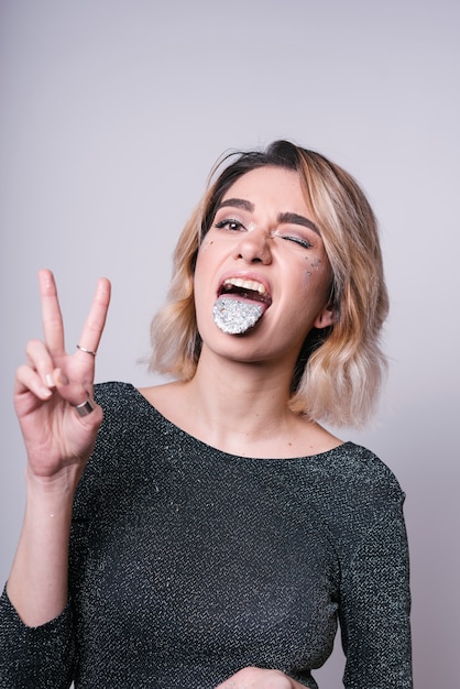 Woman with light glitter powder on tongue showing peace gesture