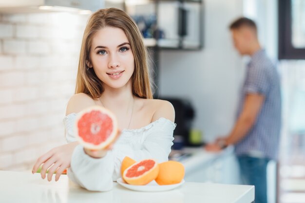 グレープフルーツの柑橘類を保持している長い髪の女の子のカラフルな目のメイクの女性