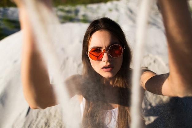 Woman with long hair in red sunglasses sits on white sand