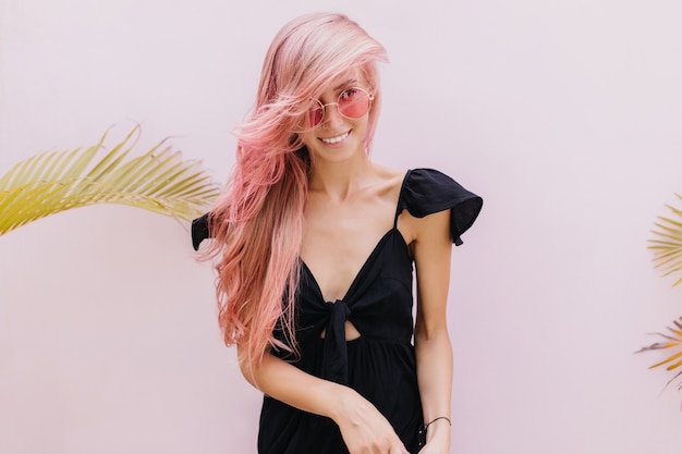 スタジオでエキゾチックなヤシの木の横に立っている長いピンクの髪の女性。