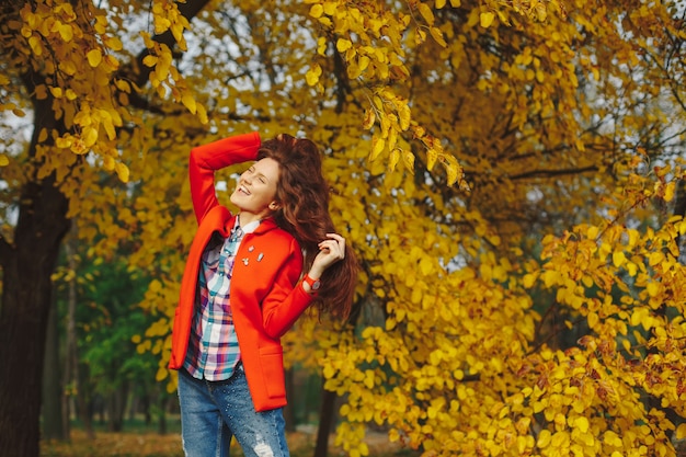 公園で秋を楽しんでいる長いウェーブのかかった髪を持つ女性。