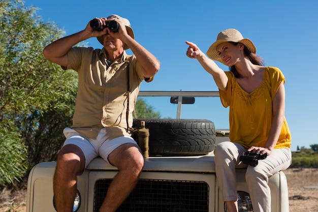 Woman with man pointing while sitting on vehicle hood