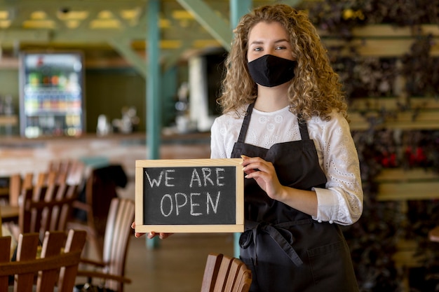 Woman with mask holding chalkboard with open sign