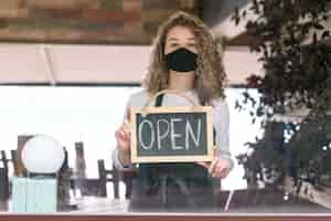 Free photo woman with mask holding chalkboard with open text