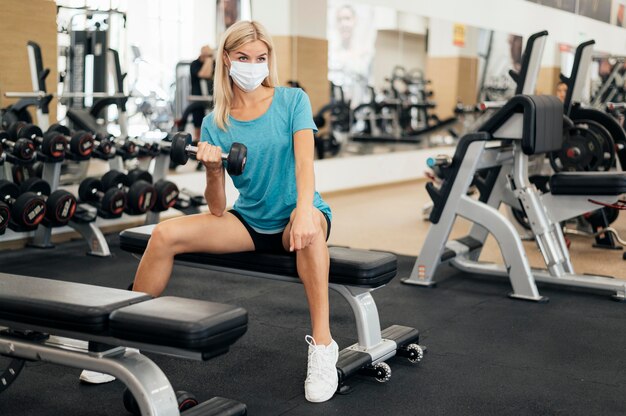 Женщина с маской тренируется в тренажерном зале во время пандемии