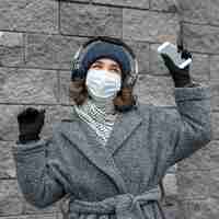 Free photo woman with medical mask in the city listening to music with headphones and smartphone