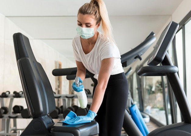 Woman with medical mask cleaning gym equipment