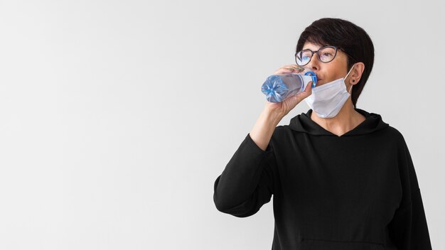 ボトルから水を飲む医療マスクを持つ女性