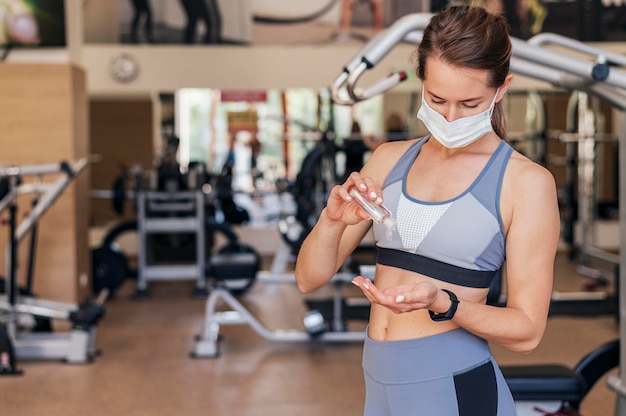 Woman with medical mask at the gym using hand sanitizer