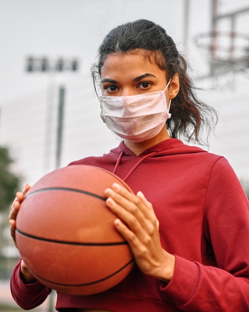 Женщина с медицинской маской держит баскетбол