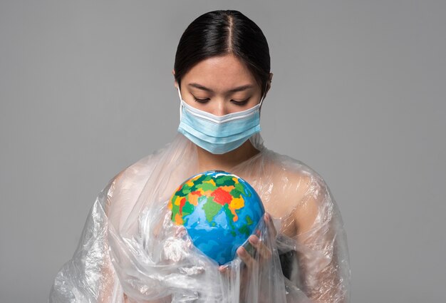 플라스틱으로 덮여있는 동안 지구 글로브를 들고 의료 마스크를 가진 여자